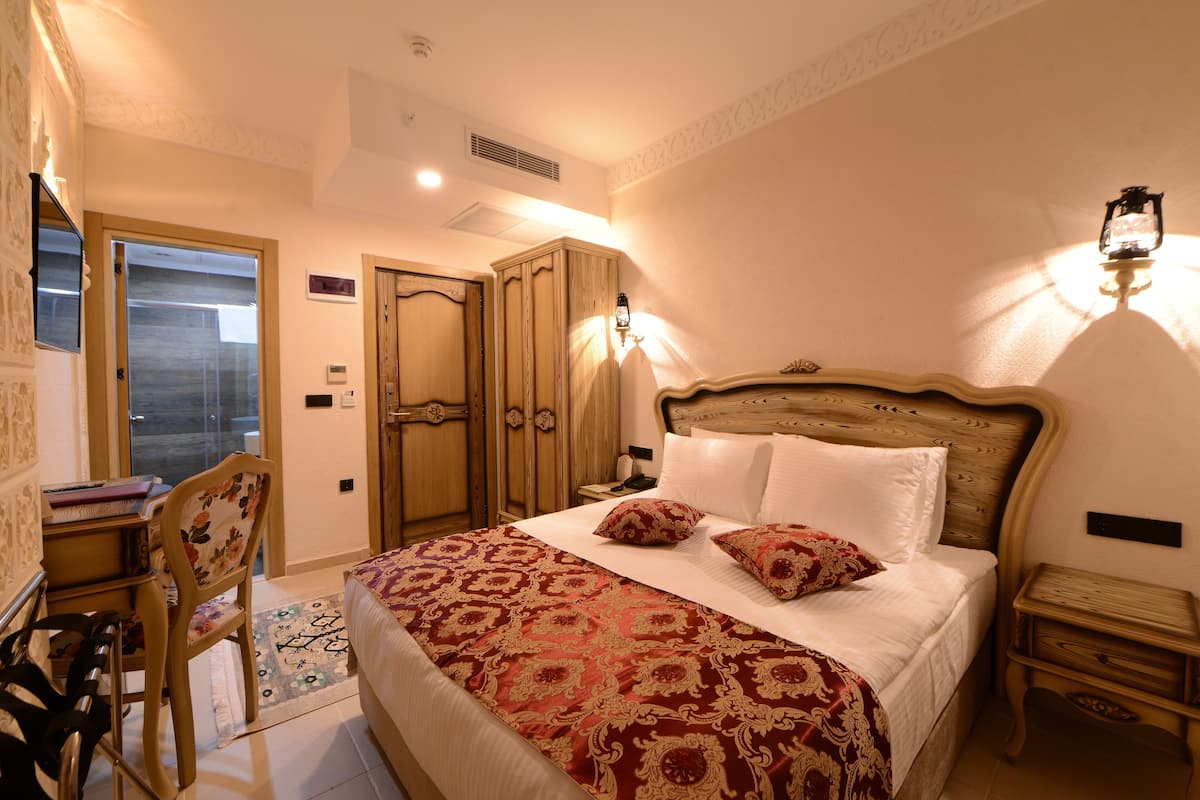 A bedroom with a large bed, a desk with a chair, a wardrobe, and a nightstand.