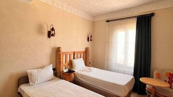 A room with two beds, a small table, a lamp, and a window with curtains.