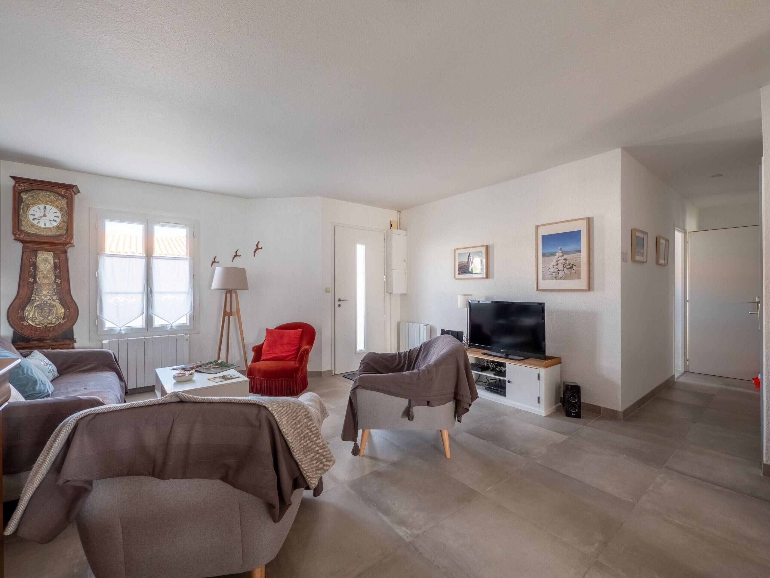 Ein Wohnzimmer mit einer großen Uhr, einem roten Sessel, einem Fernseher und einem Kamin.