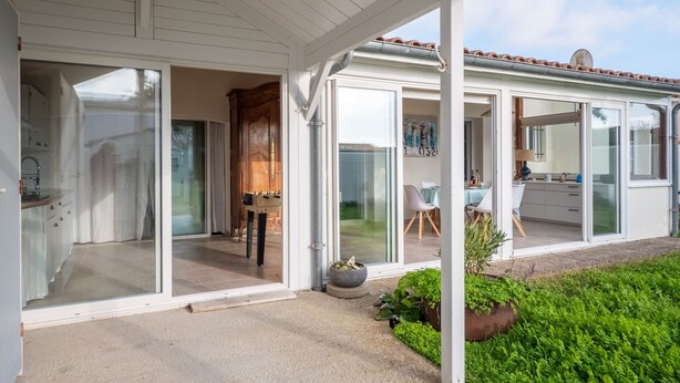 A covered patio area with sliding glass doors leading to a dining space, a kitchen area, and a small garden with potted plants. - Nice family house for 6 , St Clément des Baleines (Saint-Clément-des-Baleines)