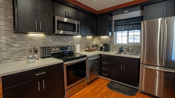 A modern kitchen with dark cabinetry, stainless steel appliances, a stone backsplash, and a wooden floor. - LuxoStays| Sleep 14! Spacious 6BR Nr Napa(10 Bed) (Fairfield)