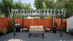 A backyard with a wooden fence, a grill, a sofa, and a table.