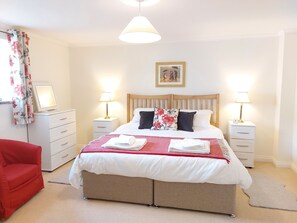 A neatly arranged bedroom with a double bed, two bedside tables with lamps, a red chair, a desk with a computer, and a framed picture on the wall. - Meadow cottage- family friendly, two bedrooms both ensuite and all on one level. (Rushyford)