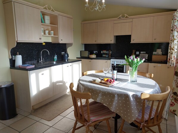 A compact kitchen with a dining area, featuring a table set with food, wine glasses, and a vase with flowers. - Meadow cottage- family friendly, two bedrooms both ensuite and all on one level. (Rushyford)