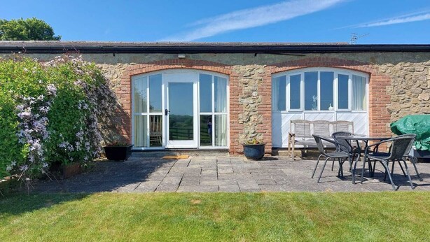 A stone building with two arched windows and a patio area with outdoor furniture. - Meadow cottage- two bedrooms both ensuite and all on one level. (Rushyford)