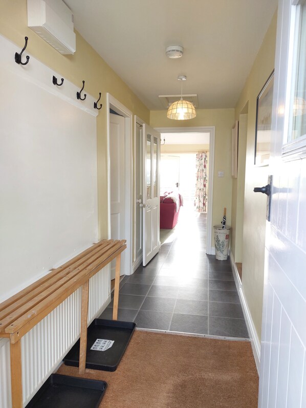 A hallway with a wooden bench, a radiator, a door with a white frame, a light fixture, and a trash can. - Meadow cottage- two bedrooms both ensuite and all on one level. (Rushyford)