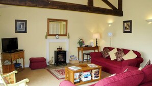 A cozy living room with a red sofa, a wooden coffee table with books, a fireplace, a television, and a wooden bench. - Meadow cottage- two bedrooms both ensuite and all on one level. (Rushyford)