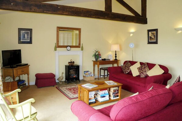 A cozy living room with a red sofa, a wooden coffee table with books, a fireplace, a television, and a wooden bench. - Meadow cottage- two bedrooms both ensuite and all on one level. (Rushyford)