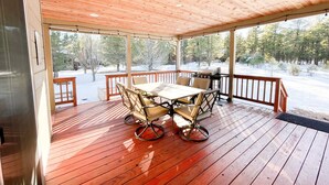 Una terraza cubierta al aire libre con una mesa y sillas de madera, una parrilla y vistas a un paisaje nevado.