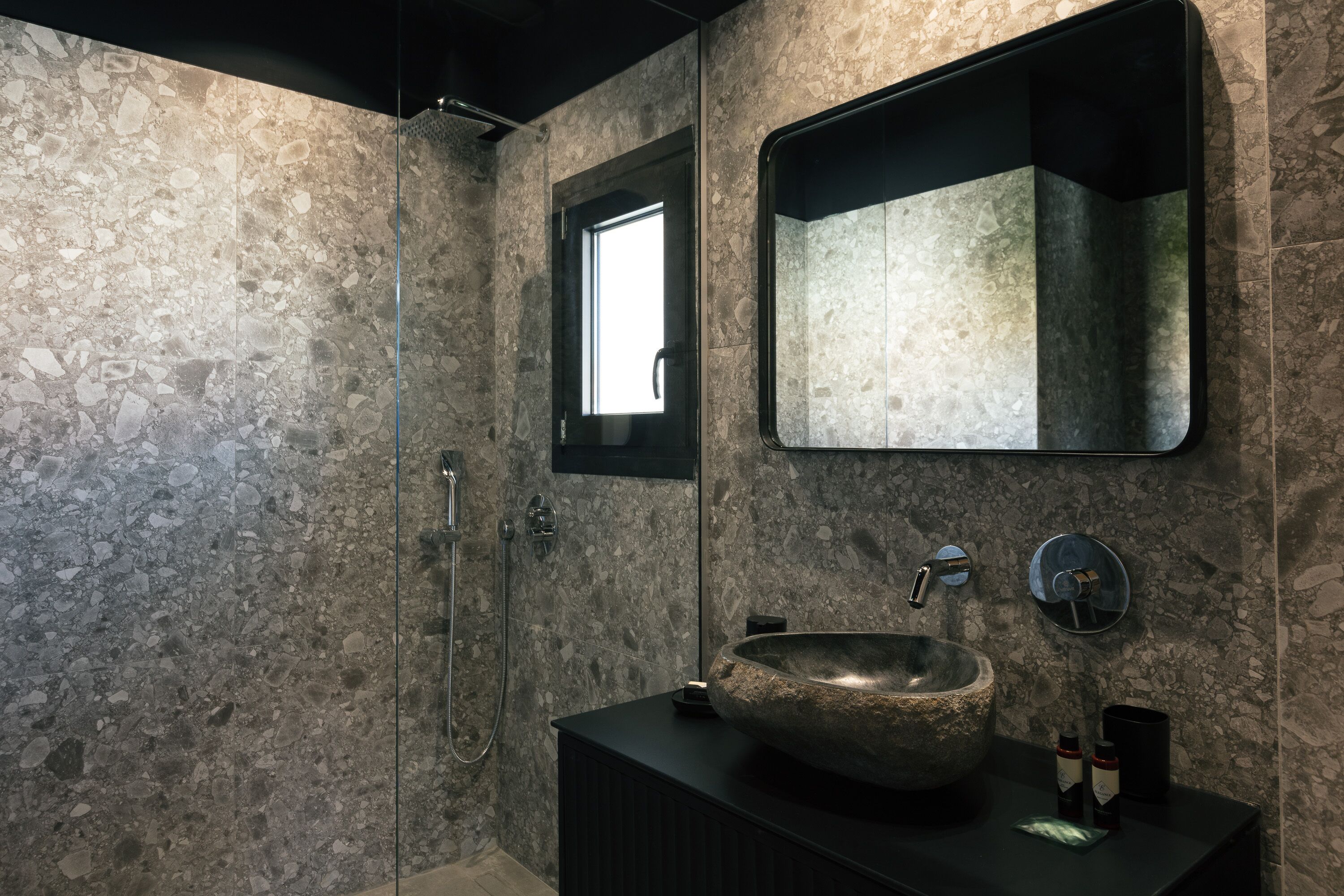 Ein Badezimmer mit einem Waschbecken aus Stein, einem Spiegel und einer Dusche.