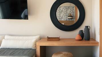 A room with a television mounted on the wall, a round mirror, a wooden console table with decorative items, and a woven basket.