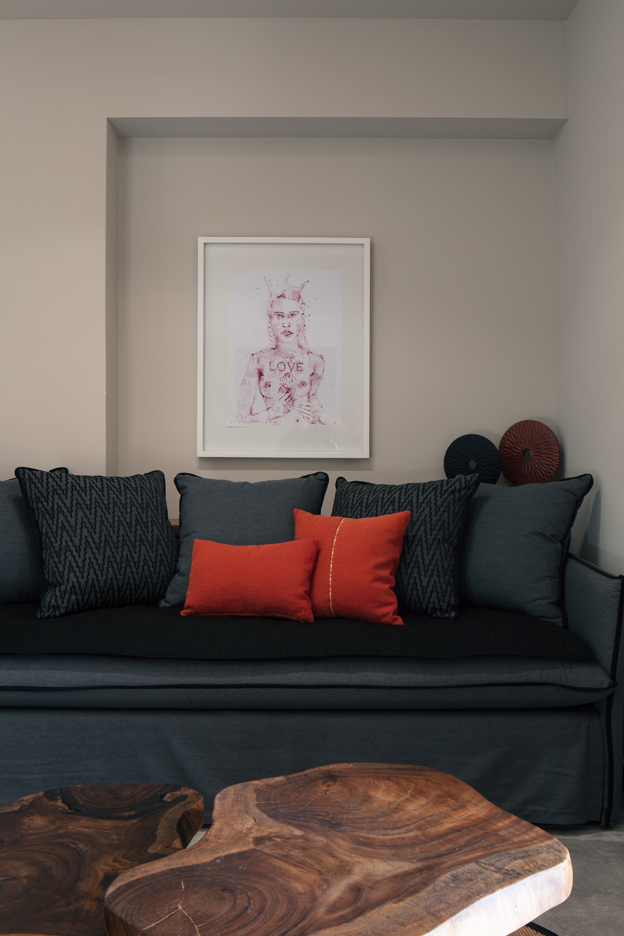 Ein stilvolles Wohnzimmer mit einem dunklen Sofa, gemusterten Kissen, einem gerahmten Kunstwerk und einem Holztisch.