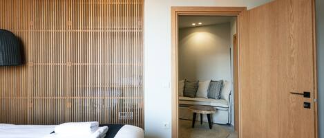A hotel room with a bed, a wooden slat wall, an air conditioning unit, and a view into the adjacent room.