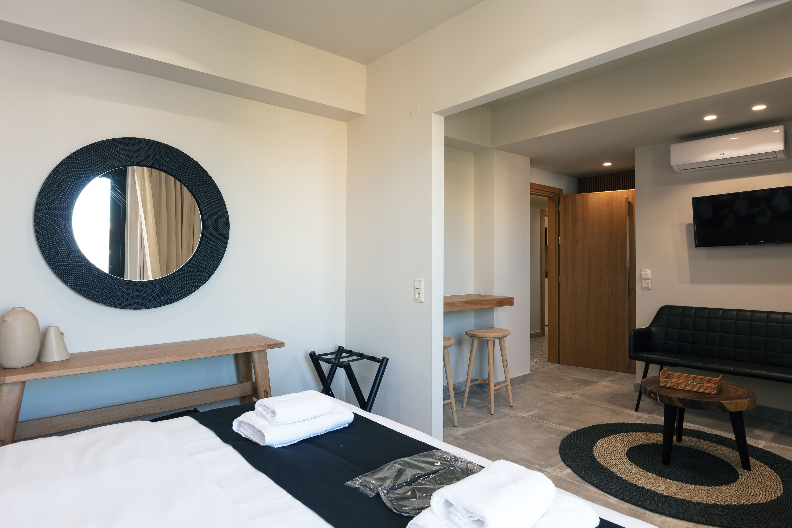 Habitación de hotel con una cama, un espejo redondo, una mesita, una silla, un sofá y un televisor.