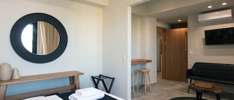 Habitación de hotel con una cama, un espejo redondo, una mesita, una silla, un sofá y un televisor.