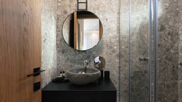A bathroom with a round mirror, a stone sink, and a shower area.