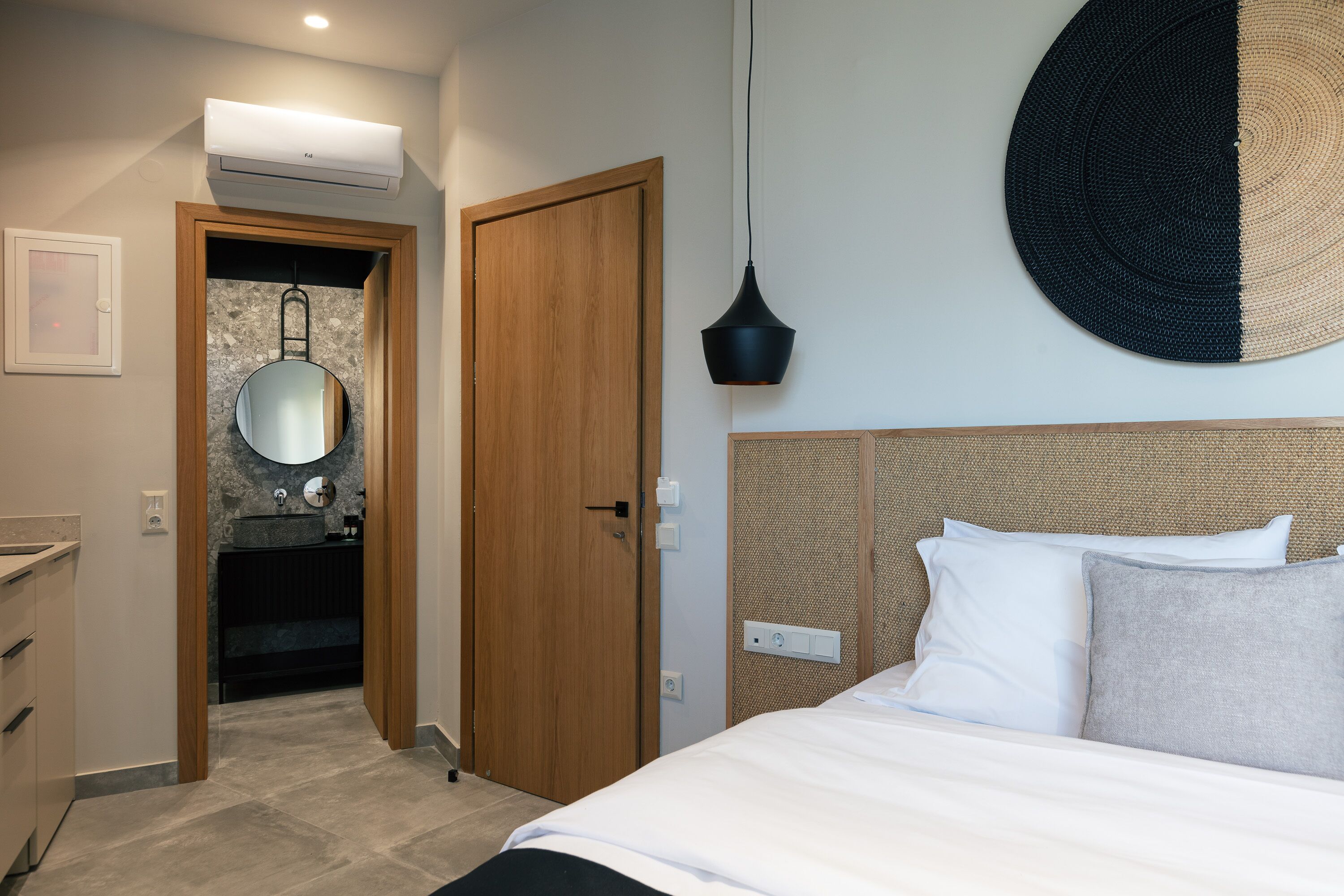 Habitació d'hotel amb llit, bany amb mirall, porta de fusta i lluminària penjada a la paret.