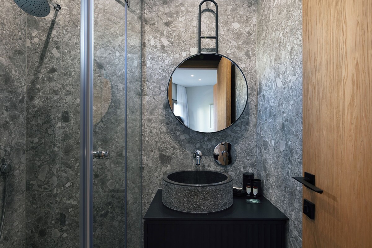 A modern bathroom with a round mirror, a circular sink, and a shower area.