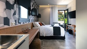 A modern hotel room with a large bed, a desk, a TV, and a view of the outdoors. - Chapter 02 Gallery Suites (Heraklion)