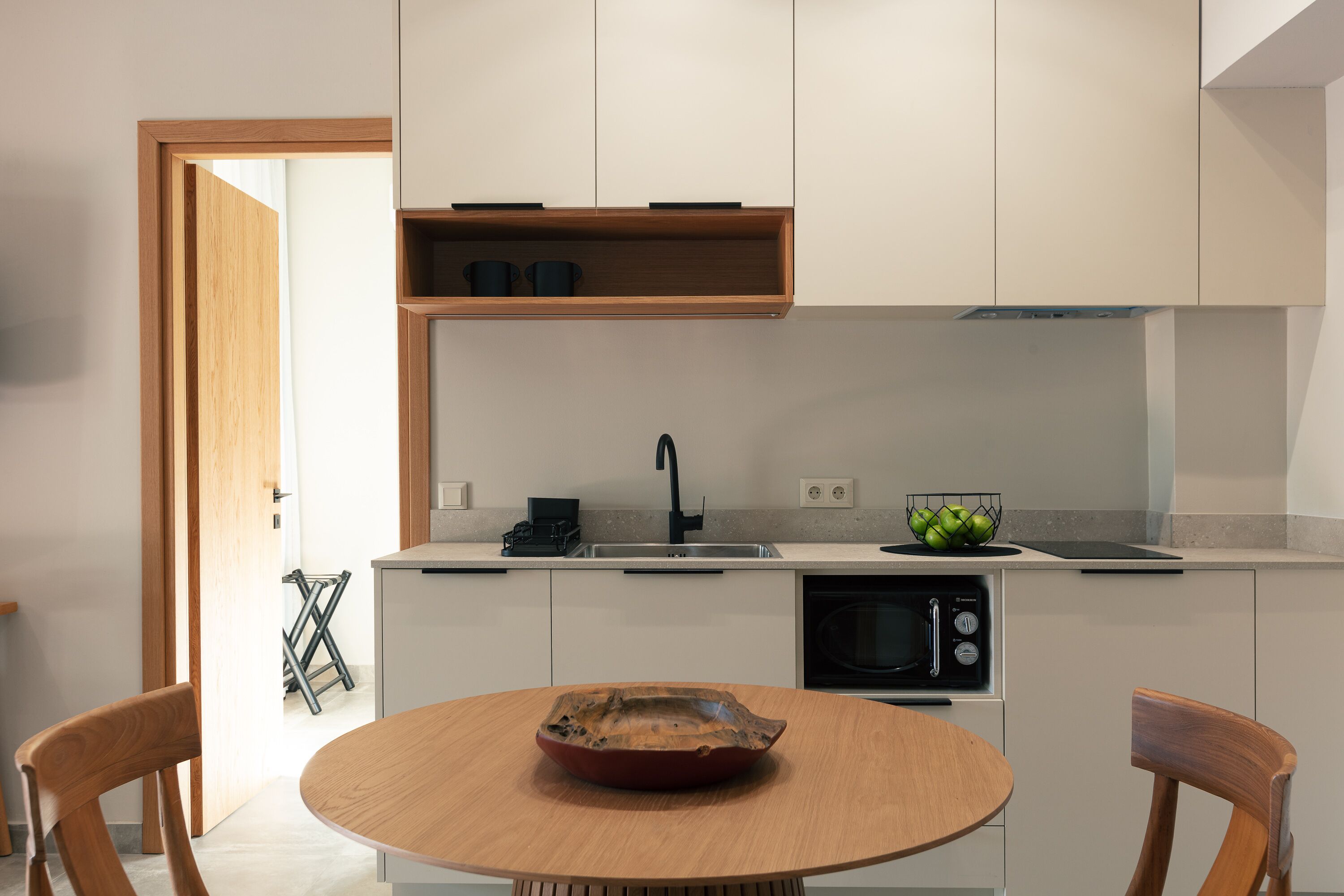 A modern kitchen with a round wooden table, built-in appliances, and a minimalist design.