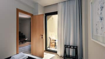 Una camera d'albergo con un letto, una sedia, un'uscita che dà su un balcone e un'ampia finestra con tende.