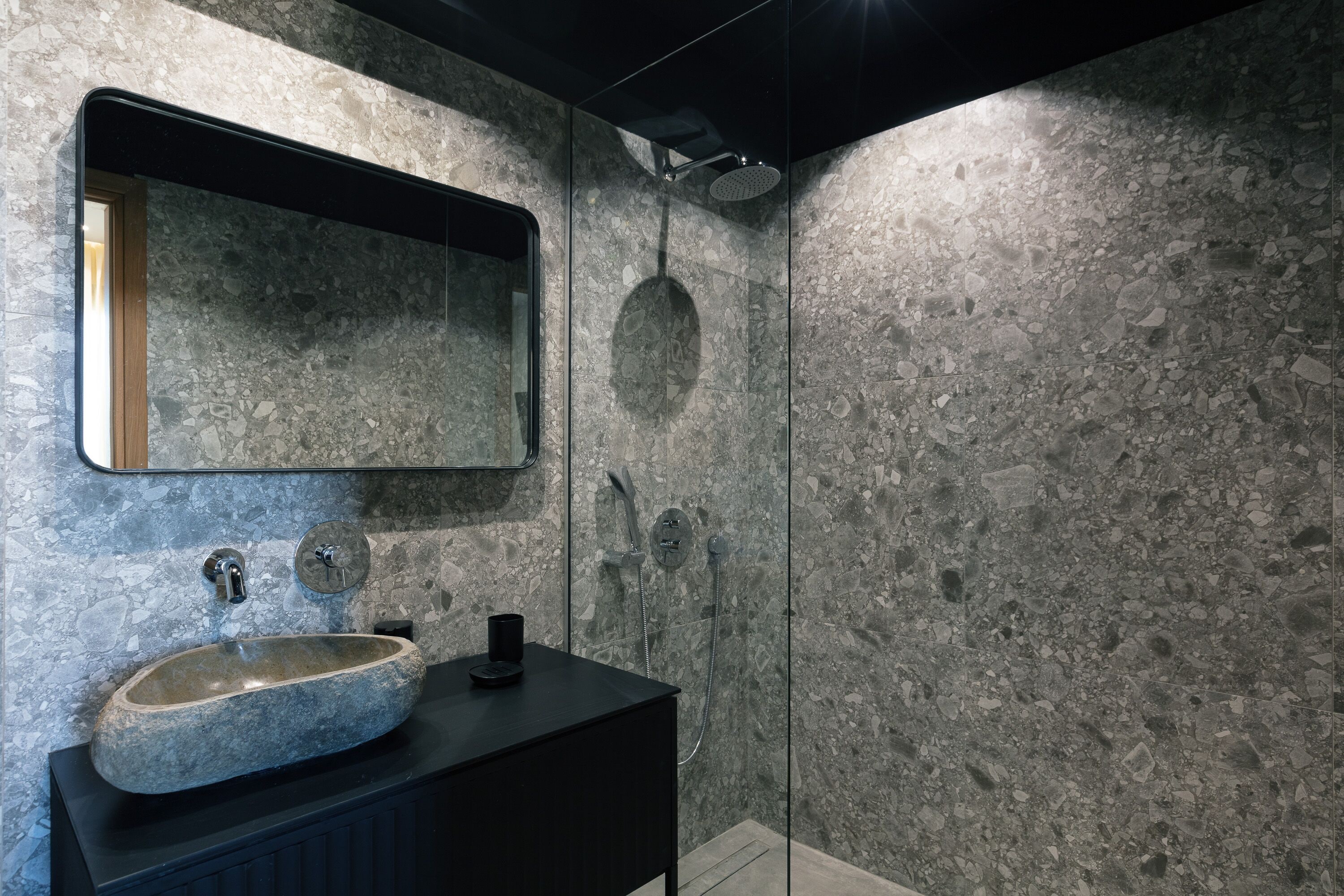 A bathroom with a stone sink, a mirror, and a shower.
