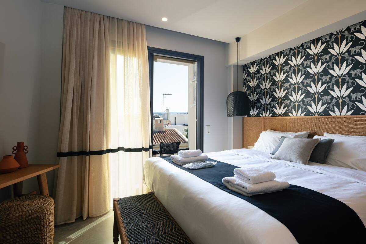 A hotel room with a bed, a view of the outside, and a patterned wall.