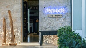 A stone building with a neon sign reading "démodé Café Bistro" and a wooden bench in the foreground. - Chapter 02 Gallery Suites (Heraklion)