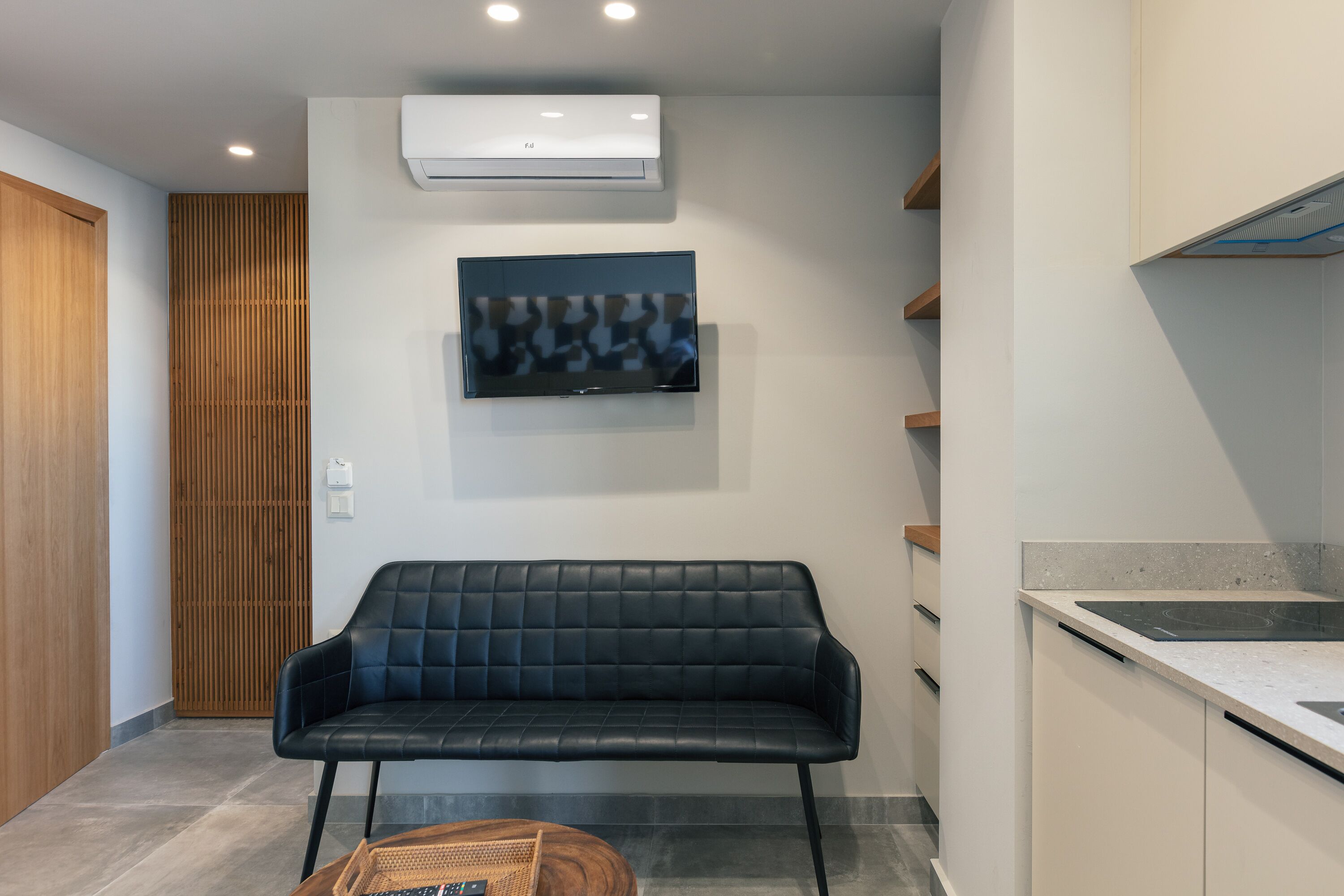 Una cocina moderna con estufa integrada, un sofá de cuero negro y un televisor de pantalla plana montado en la pared.