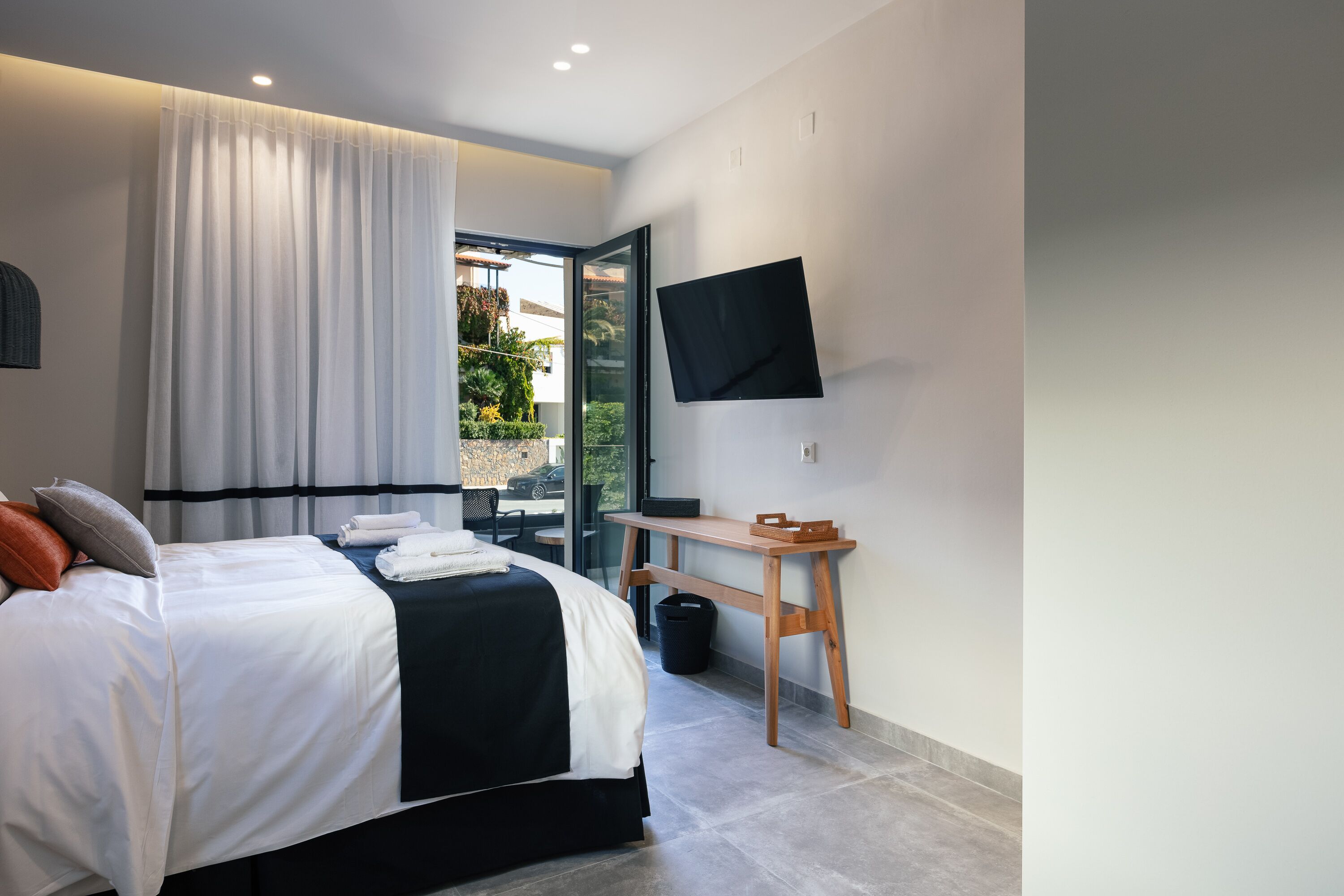 A modern hotel room with a bed, a desk, a television, and a view of the outdoors.