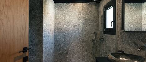 Ein modernes Badezimmer mit einem großen Becken aus Stein, einer Dusche und einer Holztür.