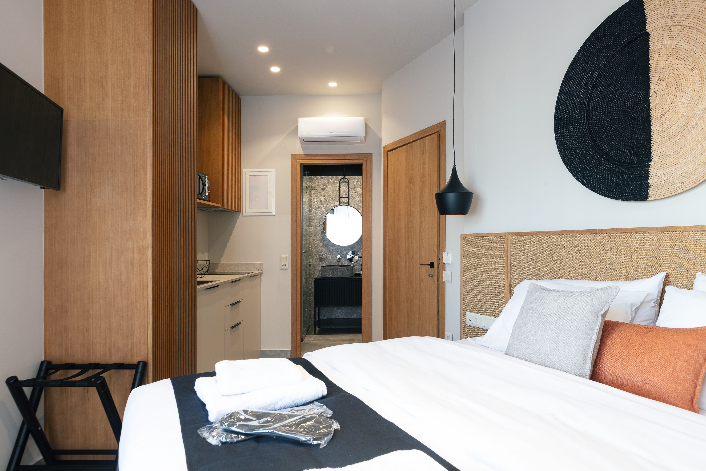 A hotel room with a bed, a desk, a mirror, and a bathroom visible through an open door.