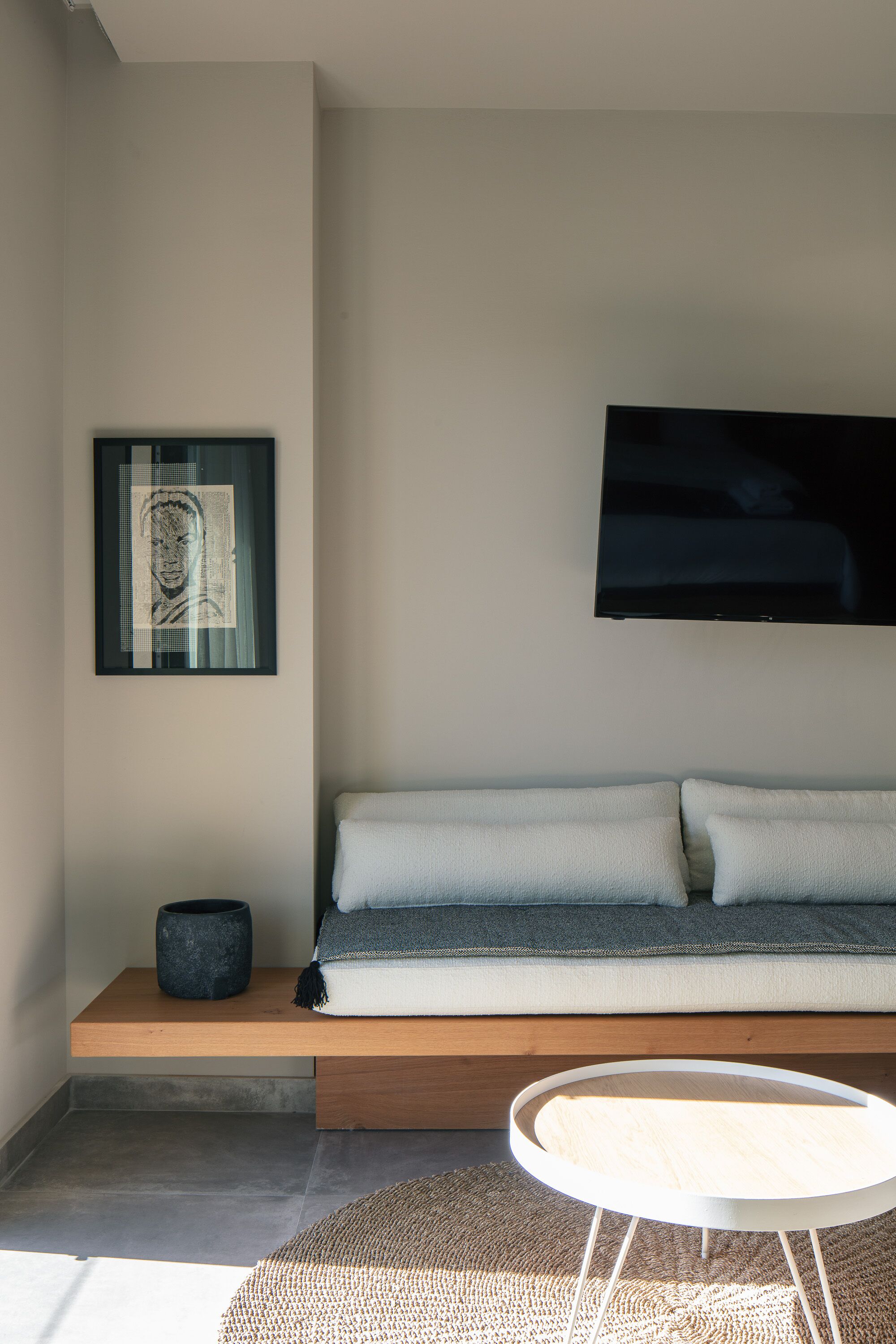 A modern living room with a sofa, a mounted flat-screen TV, a framed artwork, and a round coffee table.