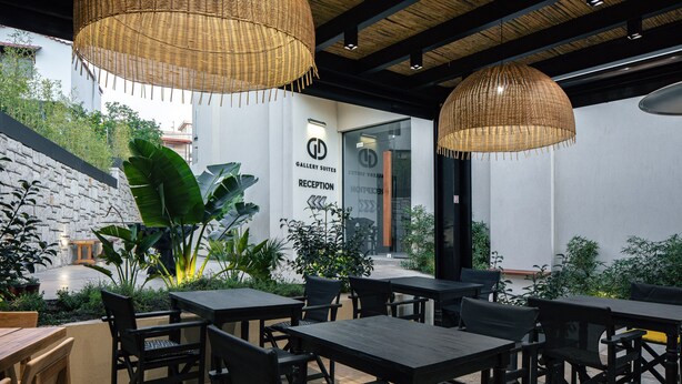 A reception area with a sign for Gallery Suites, surrounded by tables and chairs, and a green wall with plants. - Chapter 02 Gallery Suites (Heraklion)