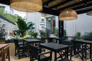 A reception area with a sign for Gallery Suites, surrounded by tables and chairs, and a green wall with plants. - Chapter 02 Gallery Suites (Heraklion)