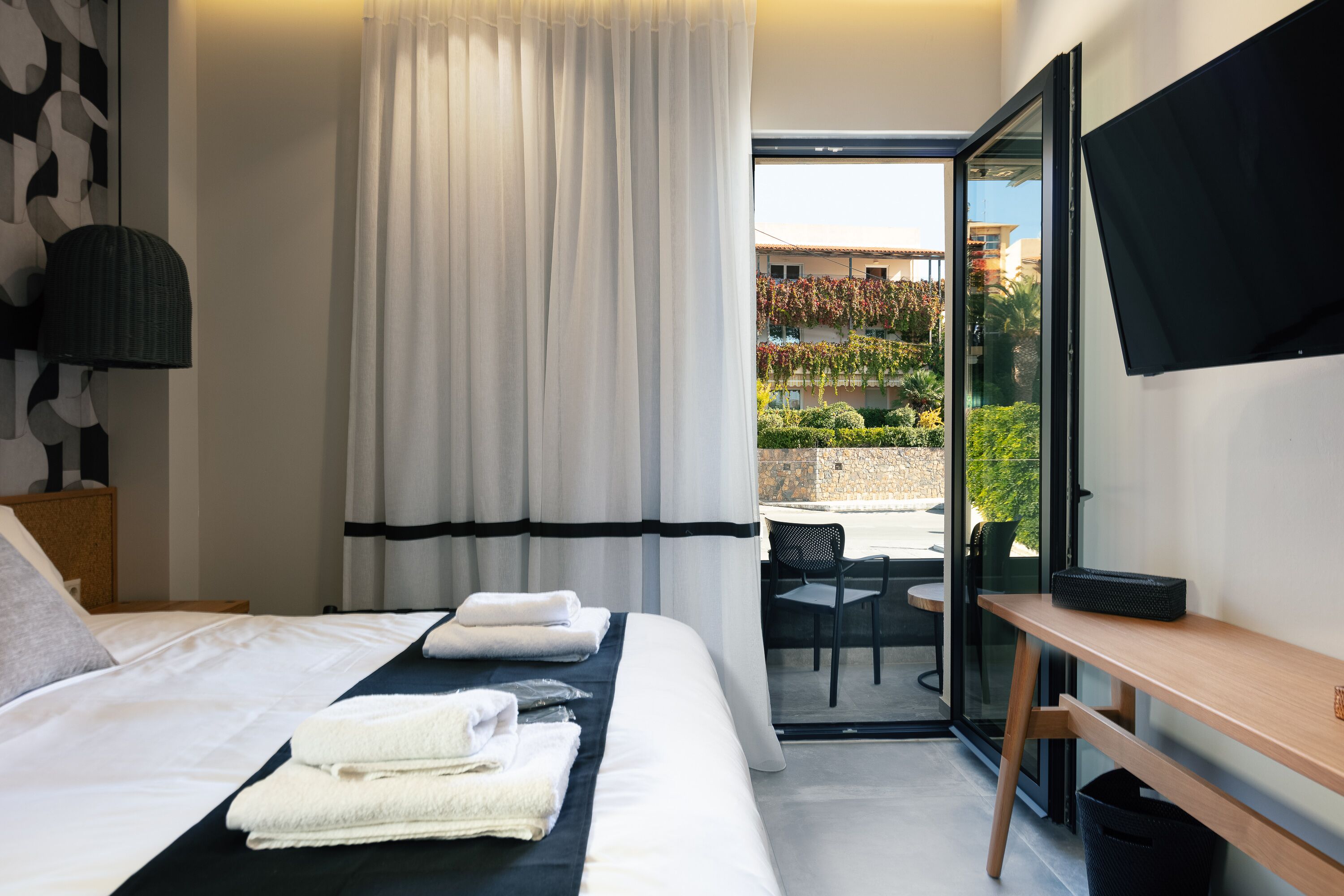 A hotel room with a bed, a desk, a chair, a TV, and a view of the outside.