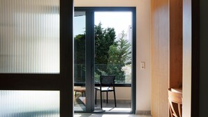 A modern room with a sliding glass door leading to a balcony with a chair and a table. - Chapter 02 Gallery Suites (Heraklion)