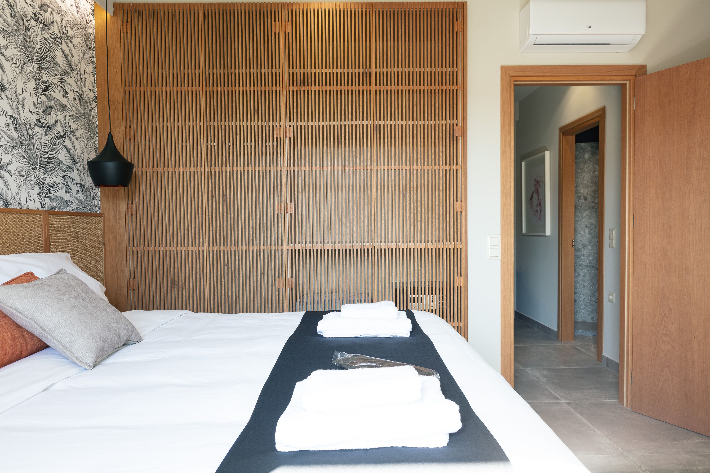 Habitación de hotel con cama, pared de listones de madera, lámpara negra y puerta que da a otra habitación.