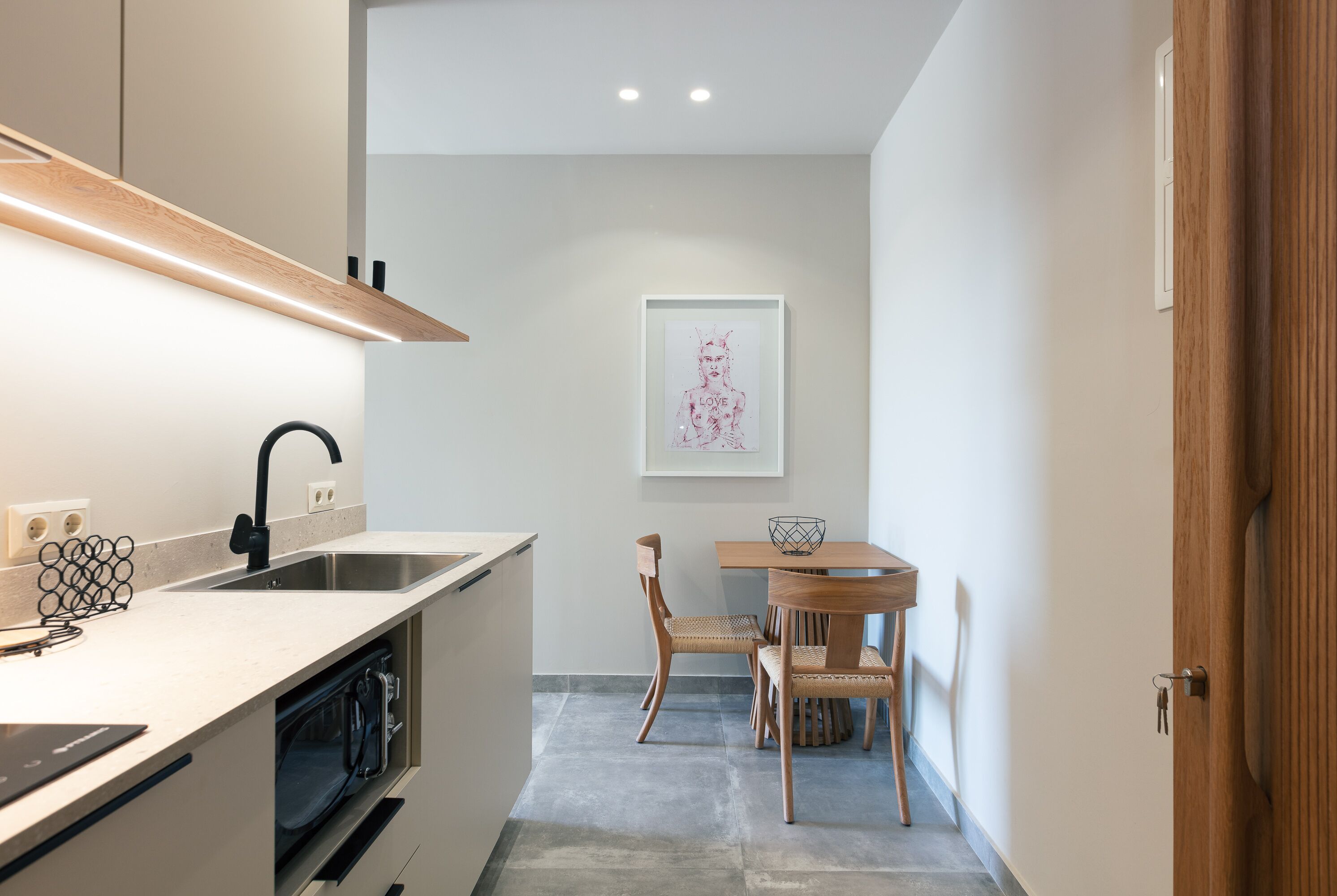 Una cocina moderna con horno empotrado, un fregadero y una zona de comedor con mesa y sillas de madera.