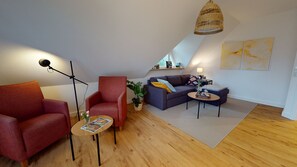 Relax in this stylish living room with a sloped ceiling, featuring a cozy armchair, sofa, and floor lamp.
