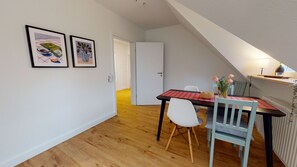 Cozy dining area with a wooden table for two, a single chair, and a small artwork on the wall.