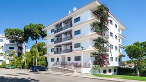 Un immeuble résidentiel à plusieurs étages, doté de balcons, d’une allée pavée et entouré de verdure.