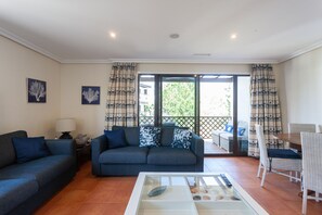 Uma sala de estar com sofá, mesa de centro de vidro e um espaço de jantar com mesa e cadeiras.