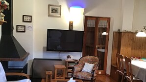A cozy living room with a fireplace, wooden furniture, a television, and a dining area with chairs and a table.