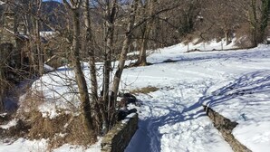 A snow-covered landscape with a stone wall and bare trees.