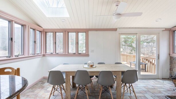 Un comedor con una mesa y sillas de madera, ventanas amplias y un ventilador de techo.