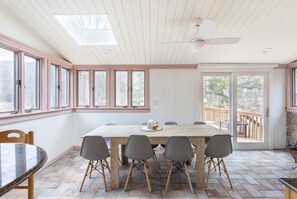 A dining area with a wooden table and chairs, large windows, and a ceiling fan.