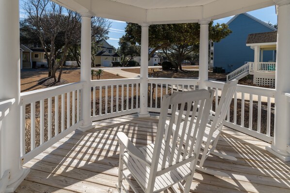 A covered porch with a wooden chair, white railings, and a view of neighboring houses.