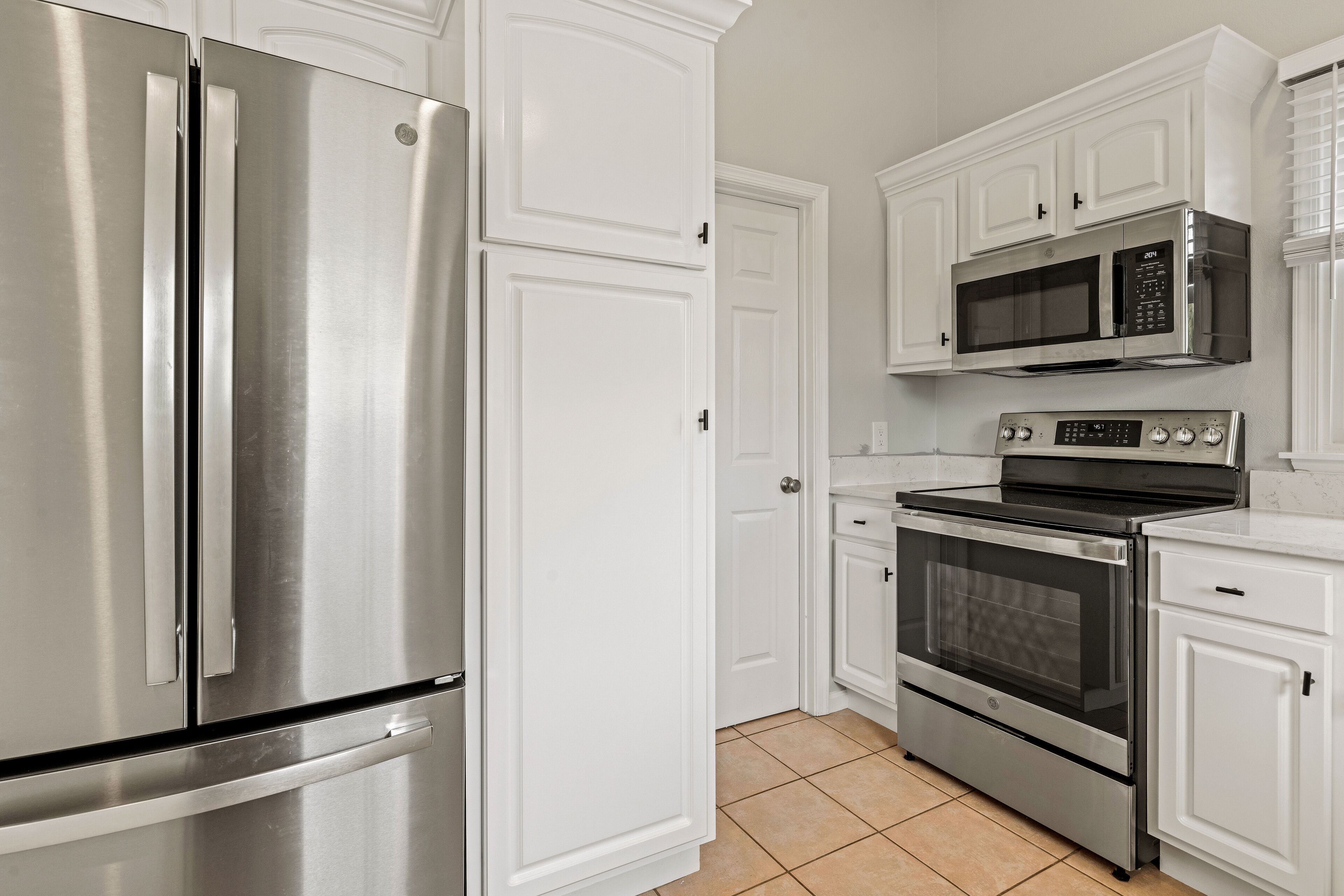 A kitchen with stainless steel appliances, white cabinetry, and a tiled floor.