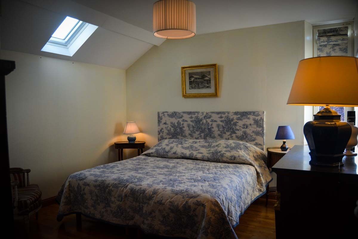 A bedroom with a skylight, a bed with a floral bedspread, a nightstand with a lamp, and a dresser with a lamp.